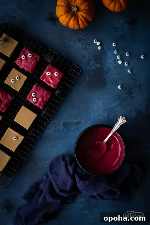 Halloween Millionaire Brownies: Rich Chocolate Caramel Treats 7 Flat lay view of Halloween millionaire brownies on a cooling rack. There is also a bowl of red white chocolate in a black bowl, a blue linen napkin, 2 small pumpkins and some edible eyes in the background. Set on a deep blue hand painted backdrop.