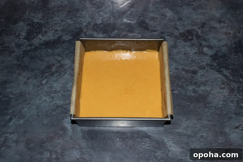 Halloween Millionaire Brownies: Rich Chocolate Caramel Treats 9 Caramel smoothed over a brownie base in a lined square baking tin on a kitchen worktop.