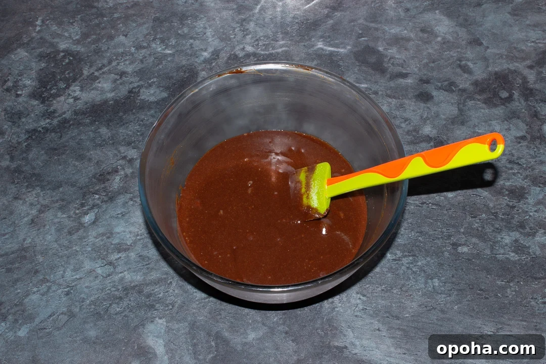 Halloween Millionaire Brownies: Rich Chocolate Caramel Treats 15 Melted dark chocolate, butter, eggs and caster sugar mixed together in a glass bowl on a kitchen worktop.