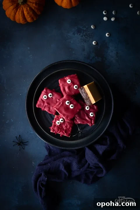 Halloween Millionaire Brownies: Rich Chocolate Caramel Treats 4 A dark blue plate filled with Halloween millionaire brownies set on a deep blue hand painted backdrop. There are also two small pumpkins, a blue linen napkin edible eyes and fake spiders in the background.