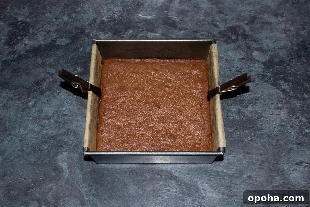 Halloween Millionaire Brownies: Rich Chocolate Caramel Treats 16 Baked brownie in a lined square baking tin on a kitchen worktop.