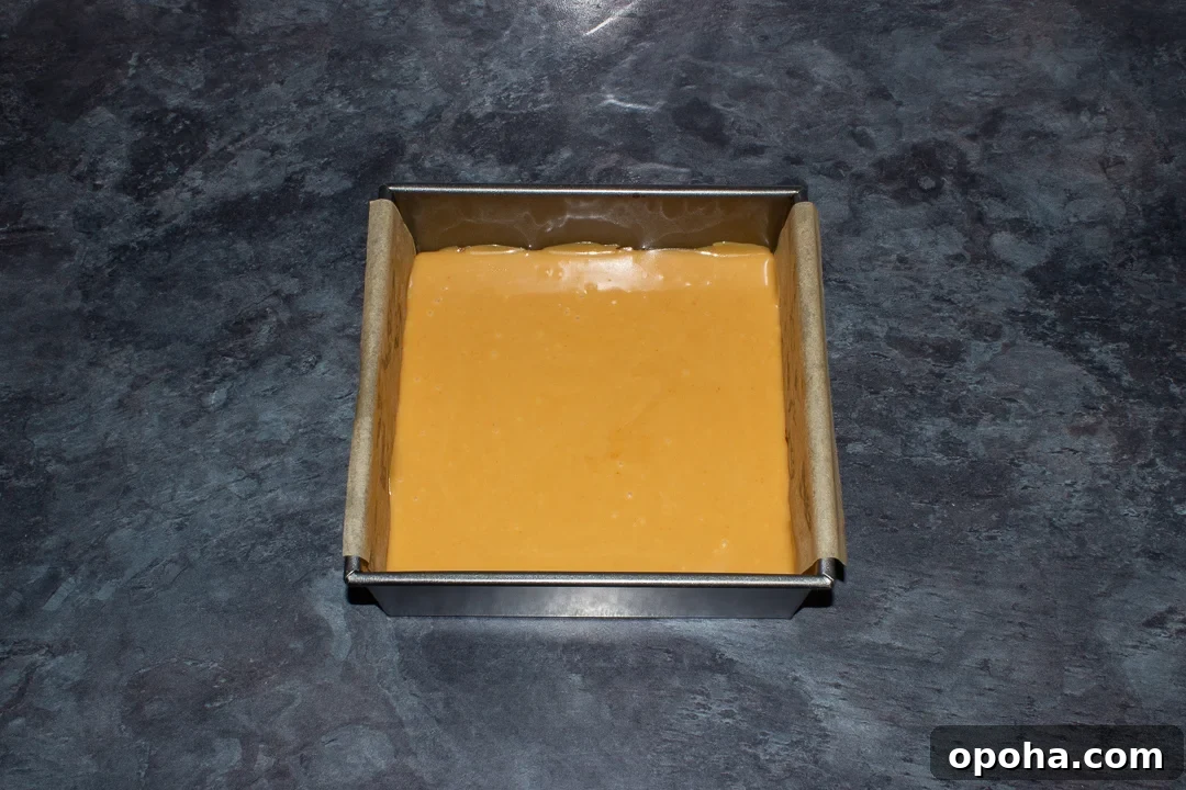 Halloween Millionaire Brownies: Rich Chocolate Caramel Treats 19 Caramel smoothed over a brownie base in a lined square baking tin on a kitchen worktop.