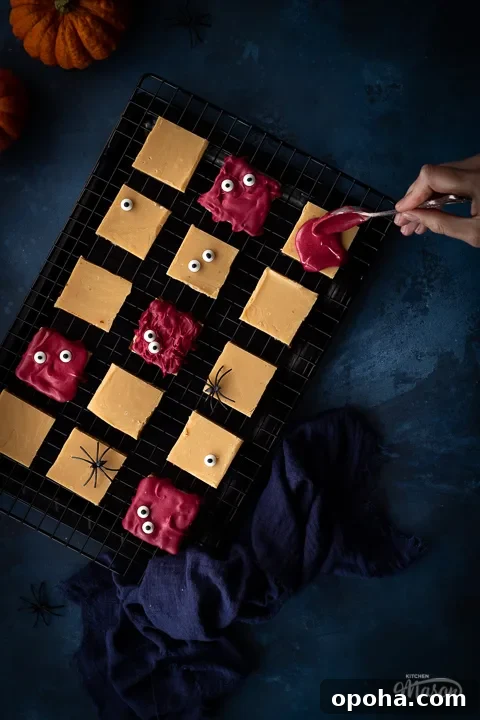 Halloween Millionaire Brownies: Rich Chocolate Caramel Treats 5 Flat lay view of Halloween millionaire brownies on a cooling rack being decorated with red white chocolate, set over a deep blue hand painted backdrop. There is also a blue linen napkin, two small pumpkins and fake spiders in the background.