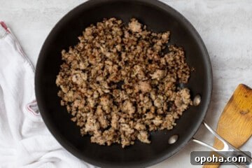 Spicy Rotel Sausage Dip Recipe for Game Day Snacks 3 Browned sausage in skillet next to wooden spoon.