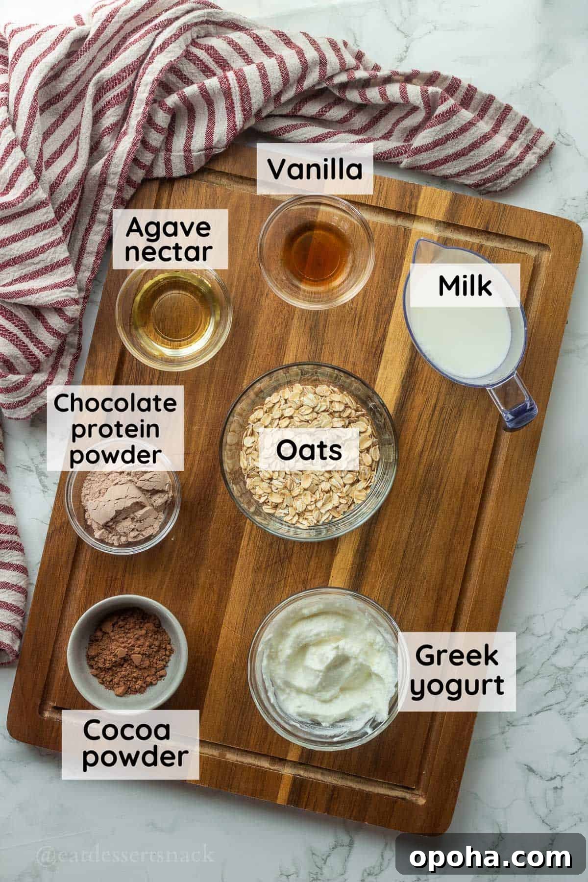 Ingredients for brownie batter overnight oats in glass bowls on wood cutting board with dish towel.
