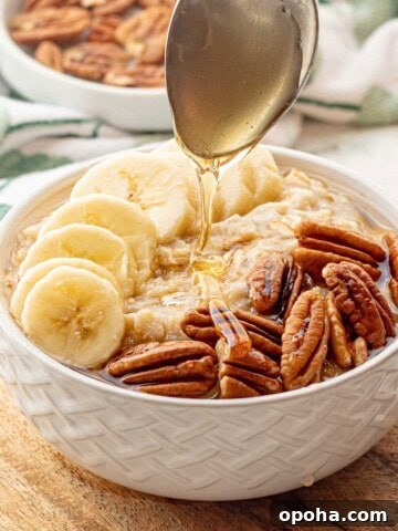 Spoon drizzling honey over white bowl of banana oatmeal.