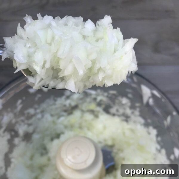 finely chopped onions on spoon hovering over onions in food processor