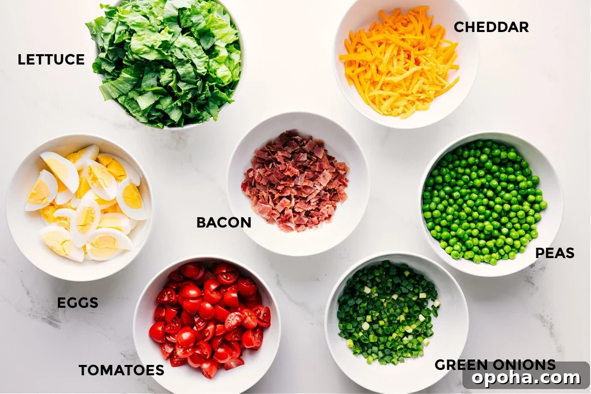 Ingredients In This 7 Layer Salad All the ingredients in this recipe prepped out for easy assembly including the lettuce, eggs, tomatoes, bacon, green onions, peas, and cheddar.