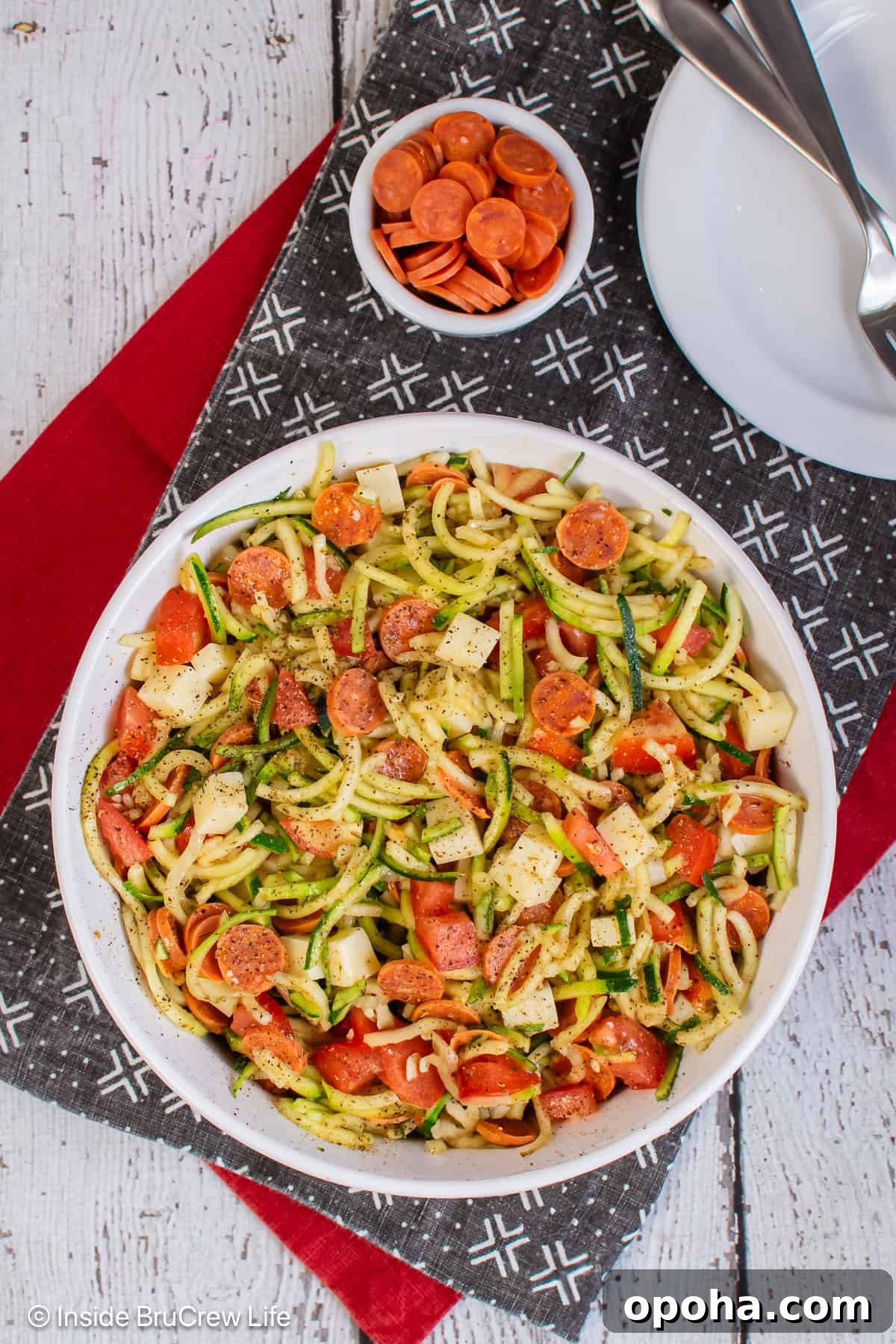 An overhead picture of a large bowl of zucchini noodle salad with pizza toppings.
