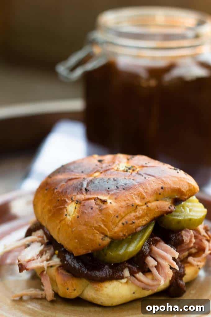 pulled pork with pumpkin spice bbq sauce between buns with pickles and jar of bbq sauce in background