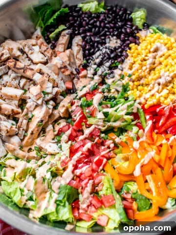 southwest salad in a large mixing bowl with black beans, corn, grilled chicken, bell peppers, tomatoes, chipotle ranch dressing, and romaine lettuce