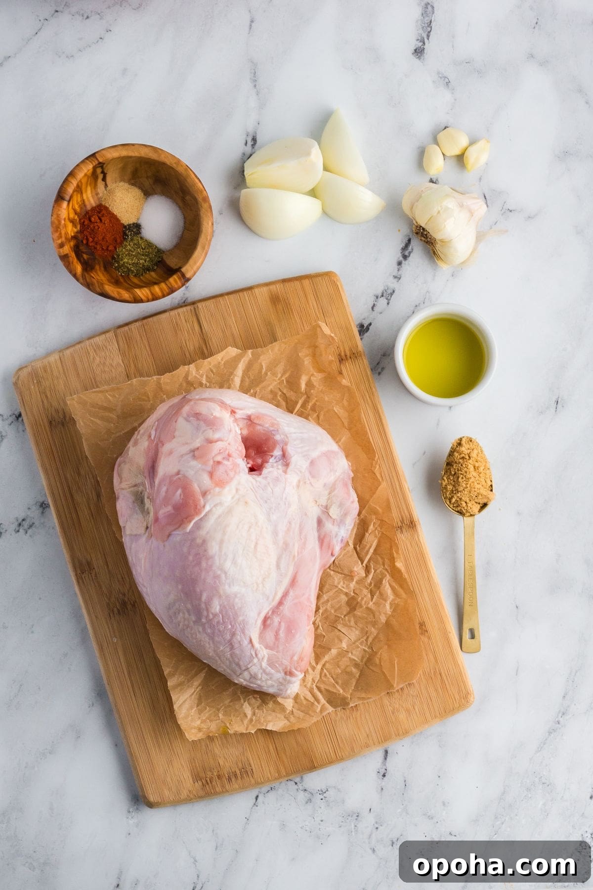 Overhead shot of ingredients for slow cooker turkey breast arranged neatly on a countertop and cutting board, including olive oil, brown sugar, spices, salt, pepper, onion, and garlic.