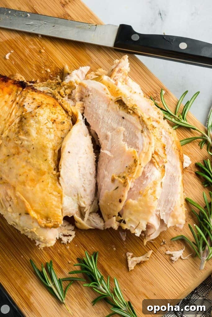 Sliced turkey breast on a wooden cutting board, showing tender, juicy meat with golden-brown crispy skin and rosemary garnish.
