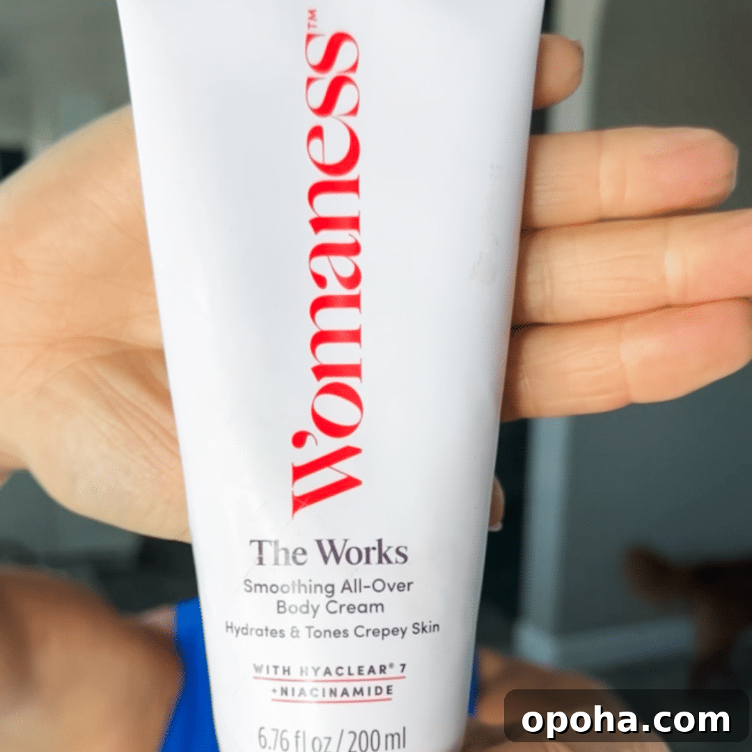 Top Anti-Aging Skincare Picks for Women Over 50 6 Woman holding up a white bottle of Womaness The Works Body Cream with hand behind it.