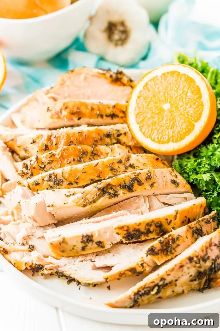 Juicy Slow-Cooker Turkey Breast Recipe for Tender Results 2 Sliced Turkey Breast with herbs on a white plate with half an orange, parsley, and garlic in the background.