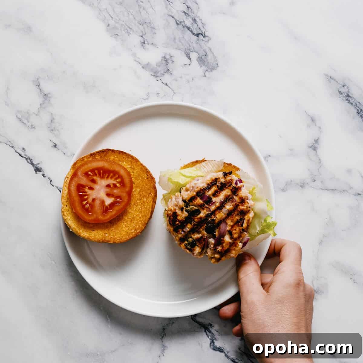 constructing a salmon burger on a white plate.