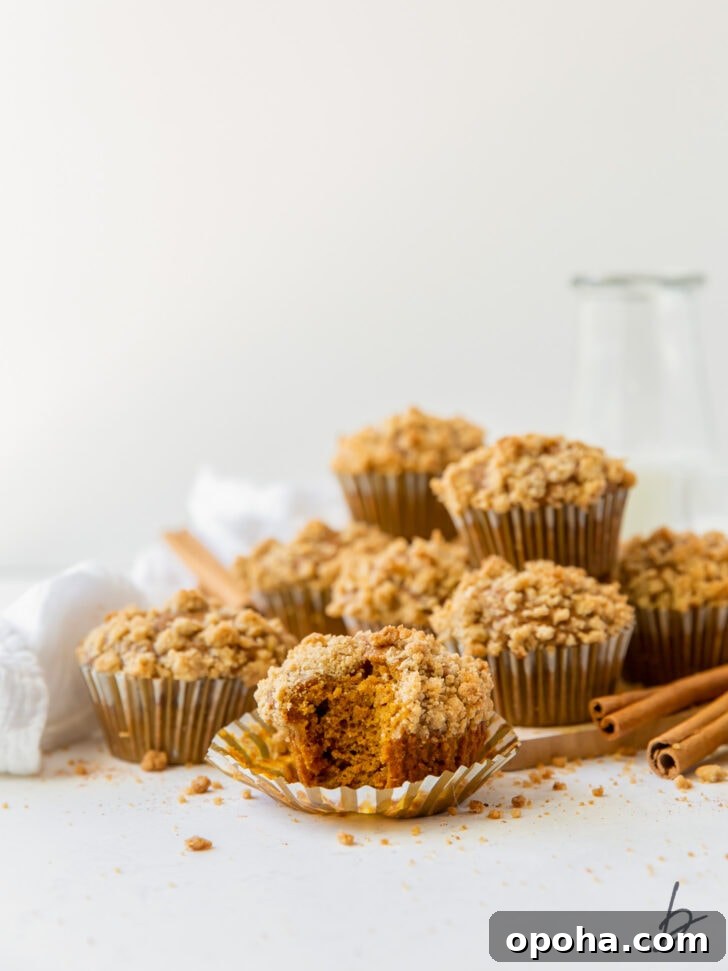 Moist Pumpkin Muffins Recipe for Fall Baking 8 pumpkin muffin with streusel on open paper liner with more muffins piled in the background