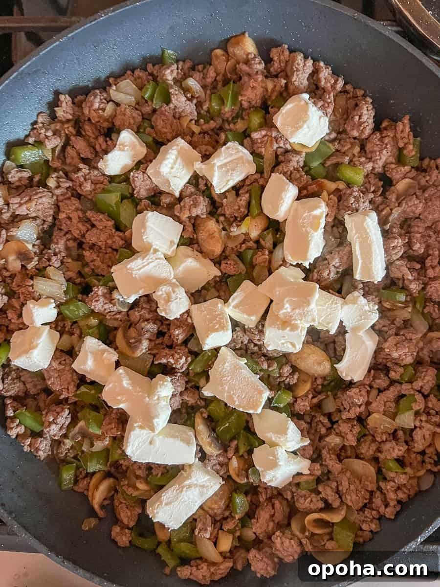 Philly Cheesesteak Casserole with Ground Beef — Savory Comfort Bake 10 Cubed cream cheese is added to the ground beef and vegetable mixture in skillet.