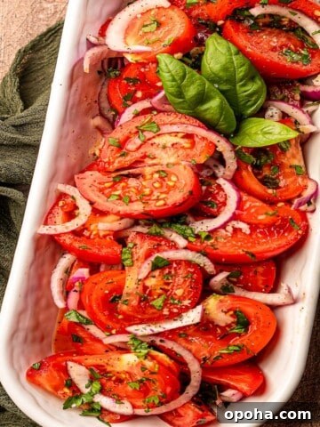 A tomato salad in a white serving dish garnished with basil.