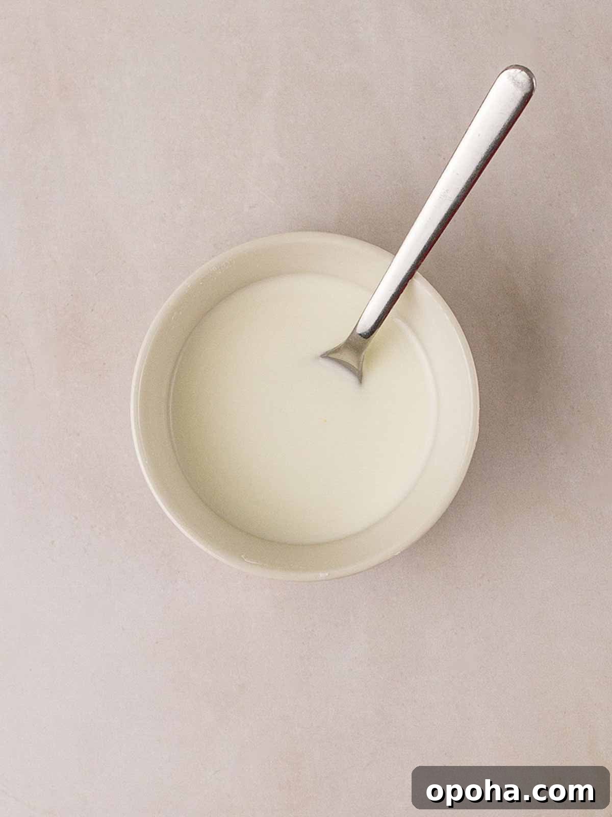 Sweet and Sour Chicken Recipe — Quick Home-Style Version 6 A small white bowl of white liquid - cornflour and water - and a spoon stirring, to thicken Sweet and Sour Chicken sauce.