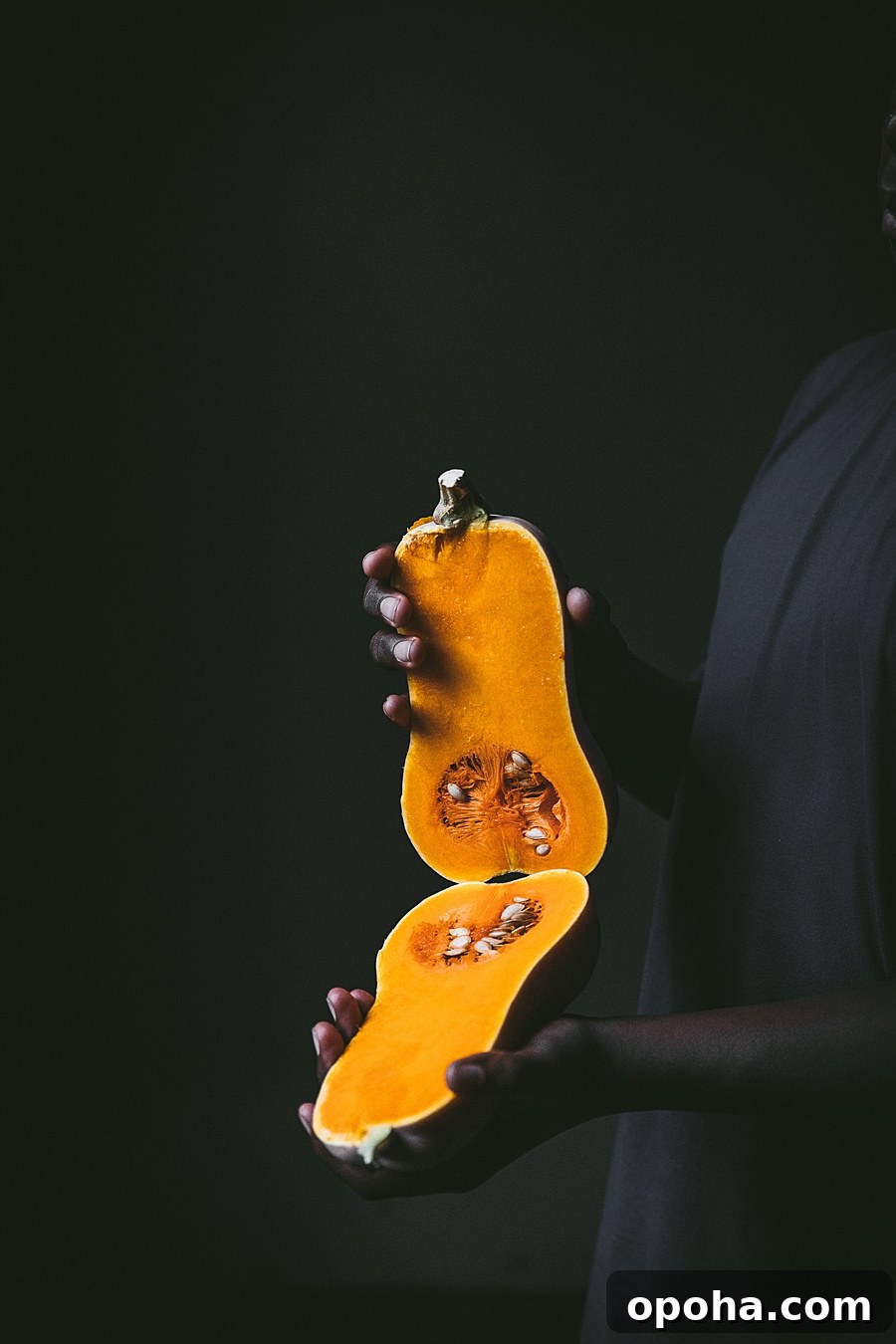 Hands holding each half of a sliced butternut squash for Soup Joumou