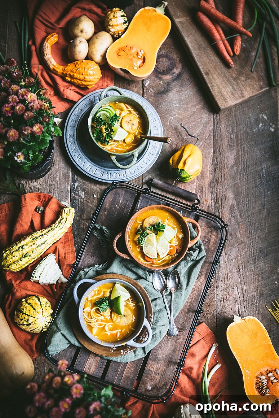 three bowls of soup joumou placed on a wooden table surrounded by other squashes