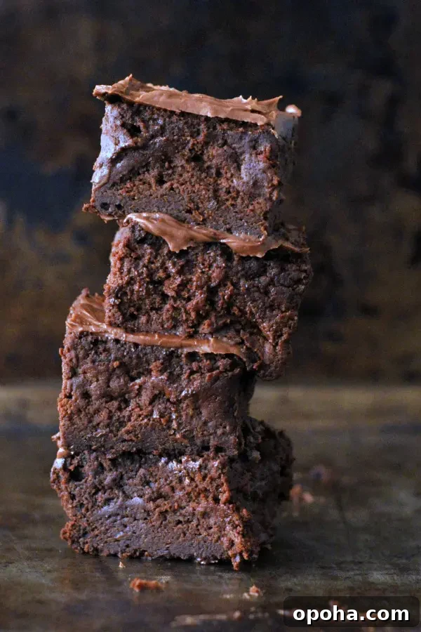 a stack of four frosted vegan brownies against a dark marbled background, the text of 'the best vegan brownies' in lower left corner