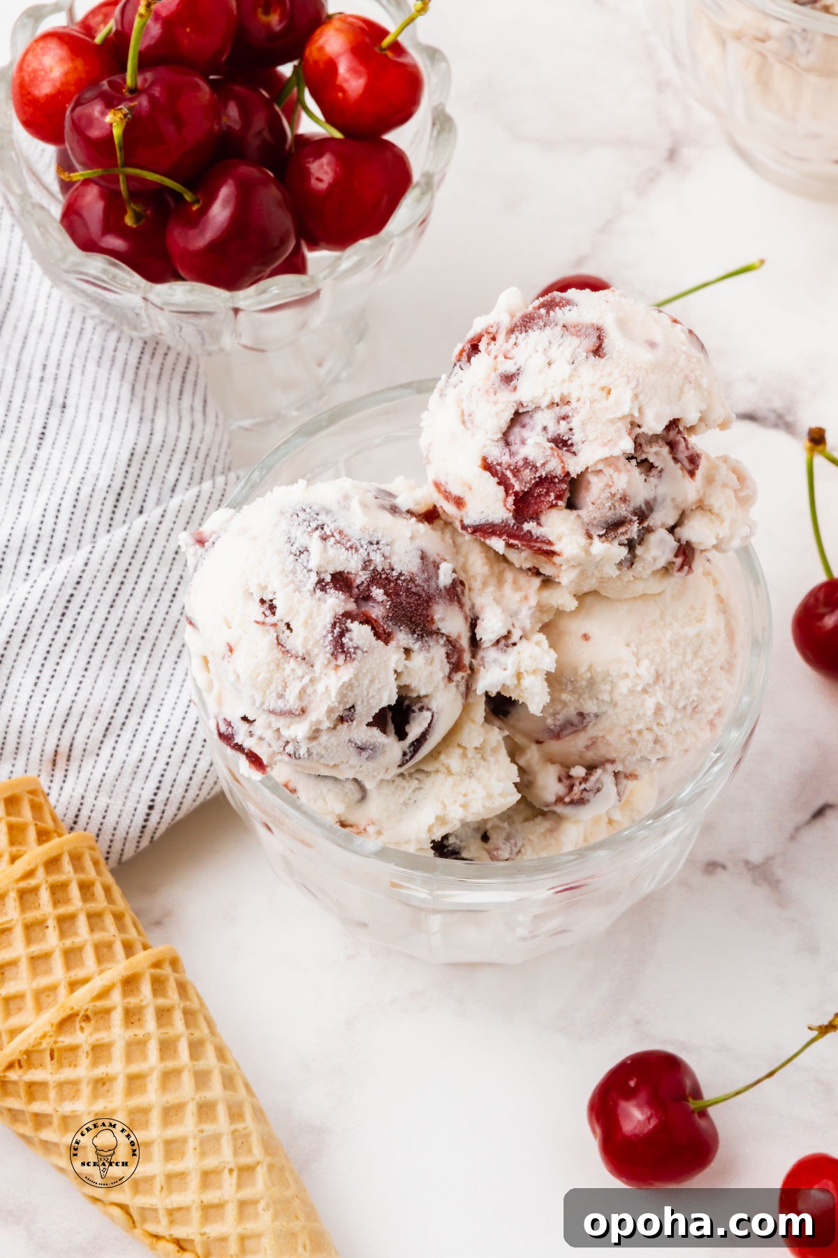 Cherry Gelato Recipe: Creamy Homemade Gelato with Fresh Cherries 6 a glass bowl filled with scoops of cherry gelato, next to a bowl of fresh cherries and sugar cones.