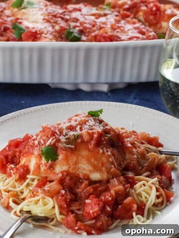 Chicken caccitore on a noodles, on a white plate with a glass of wine and a casserole dish of more chicken caccitore in background