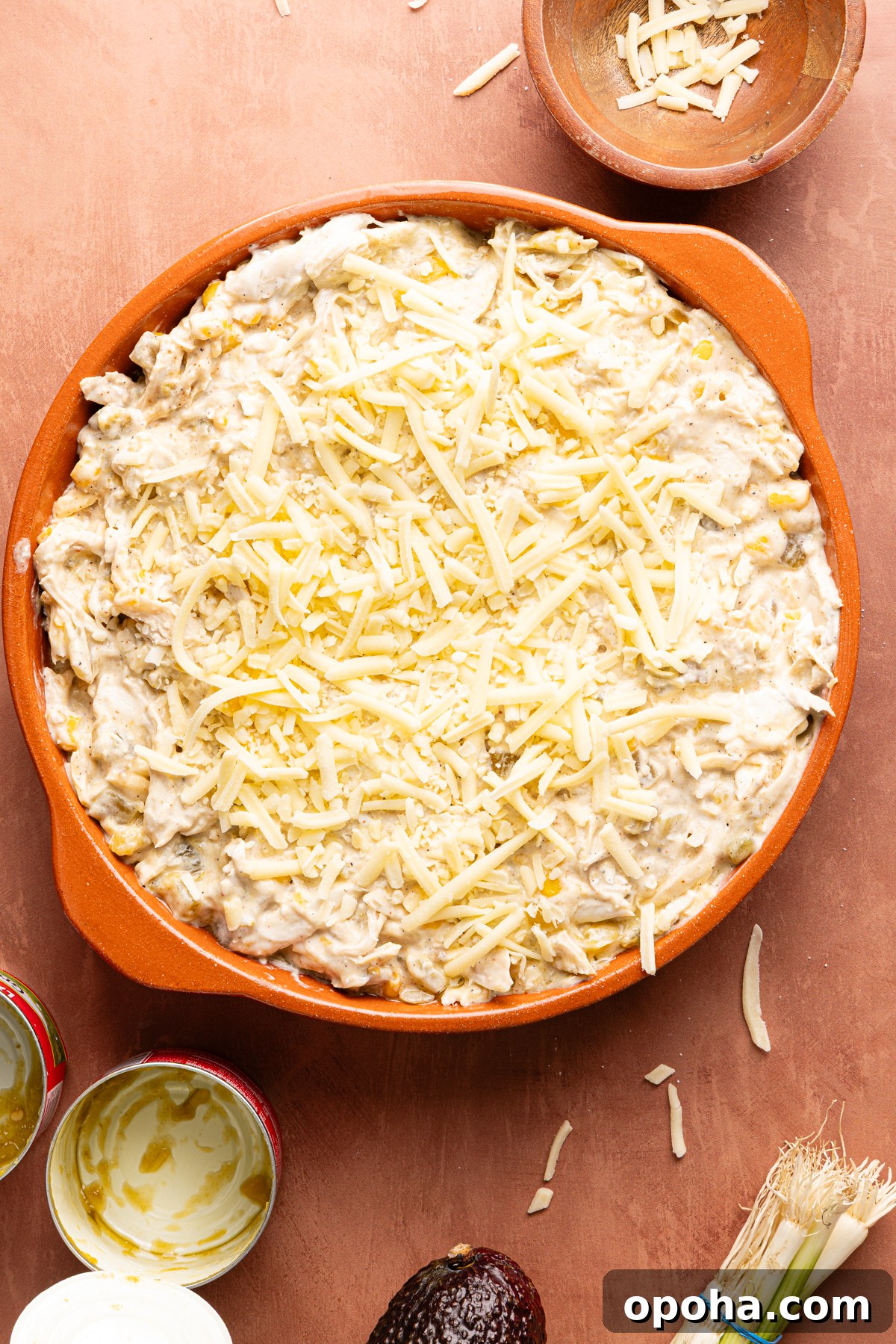 A round baking dish filled with green chile chicken enchilada dip garnished with shredded cheese