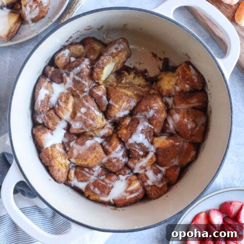 dutch oven with fully cooked monkey bread with a caramelized outer layer with cream cheese glaze over the top