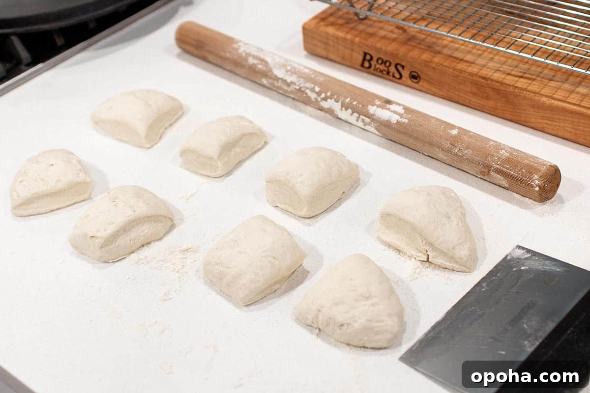 Sourdough Discard Naan Recipe: Crispy, Chewy Flatbread 5 A loaf of dough divided into 8 pieces getting ready to be rolled out. With a bench scraper and rolling pin.