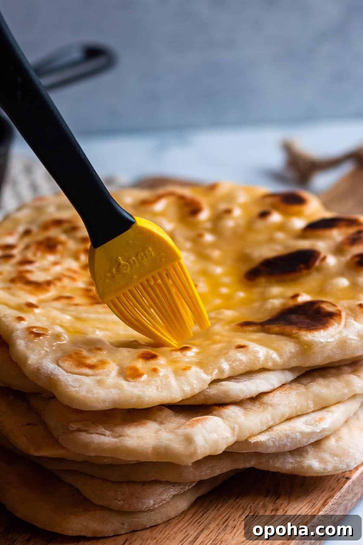 Sourdough Discard Naan Recipe: Crispy, Chewy Flatbread 8 A stack of freshly cooked sourdough naan with a brush spreading on melted butter.