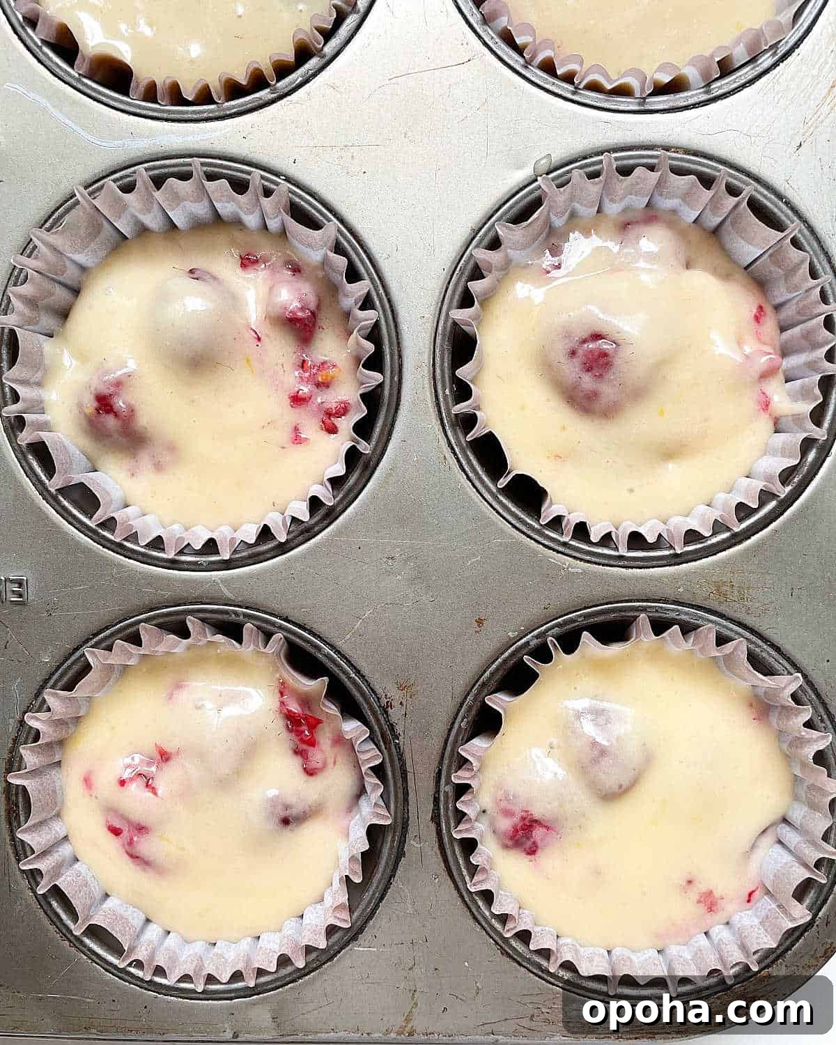 Quick Raspberry Muffins Recipe — Light, Tangy, Perfect for Brunch 9 Close up of unbaked raspberry muffins in paper liner in a metal pan.