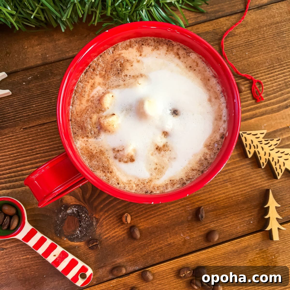 Homemade Mocha Coffee Bombs: Decadent Hot Chocolate Surprise 2 A red mug of hot chocolate topped with steamed milk on a wooden background surrounded by spilled coffee beans.