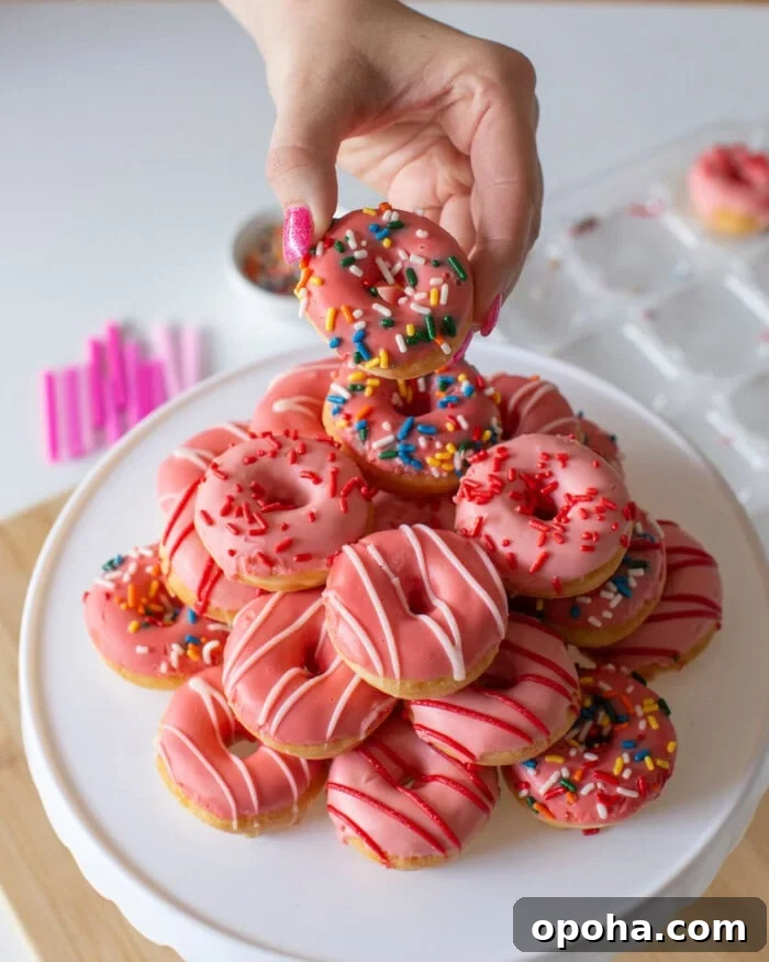 Donut Cake Tower Ideas: Show-Stopping Dessert Centerpieces 8 A hand holding a small pink frosted donut with colorful sprinkles, above a plate stacked with similar donuts.