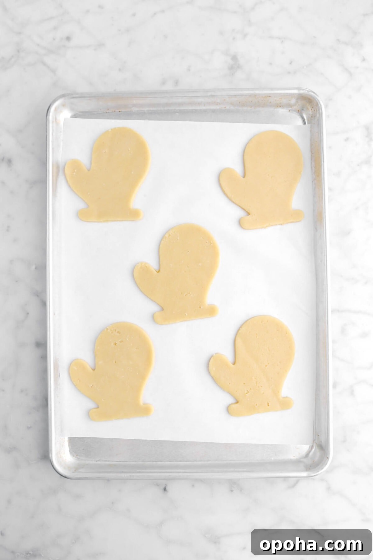Santa’s Glove Peppermint Sugar Cookies: Festive Holiday Recipe 13 five unbaked glove shaped cookies on parchment lined sheet pan.