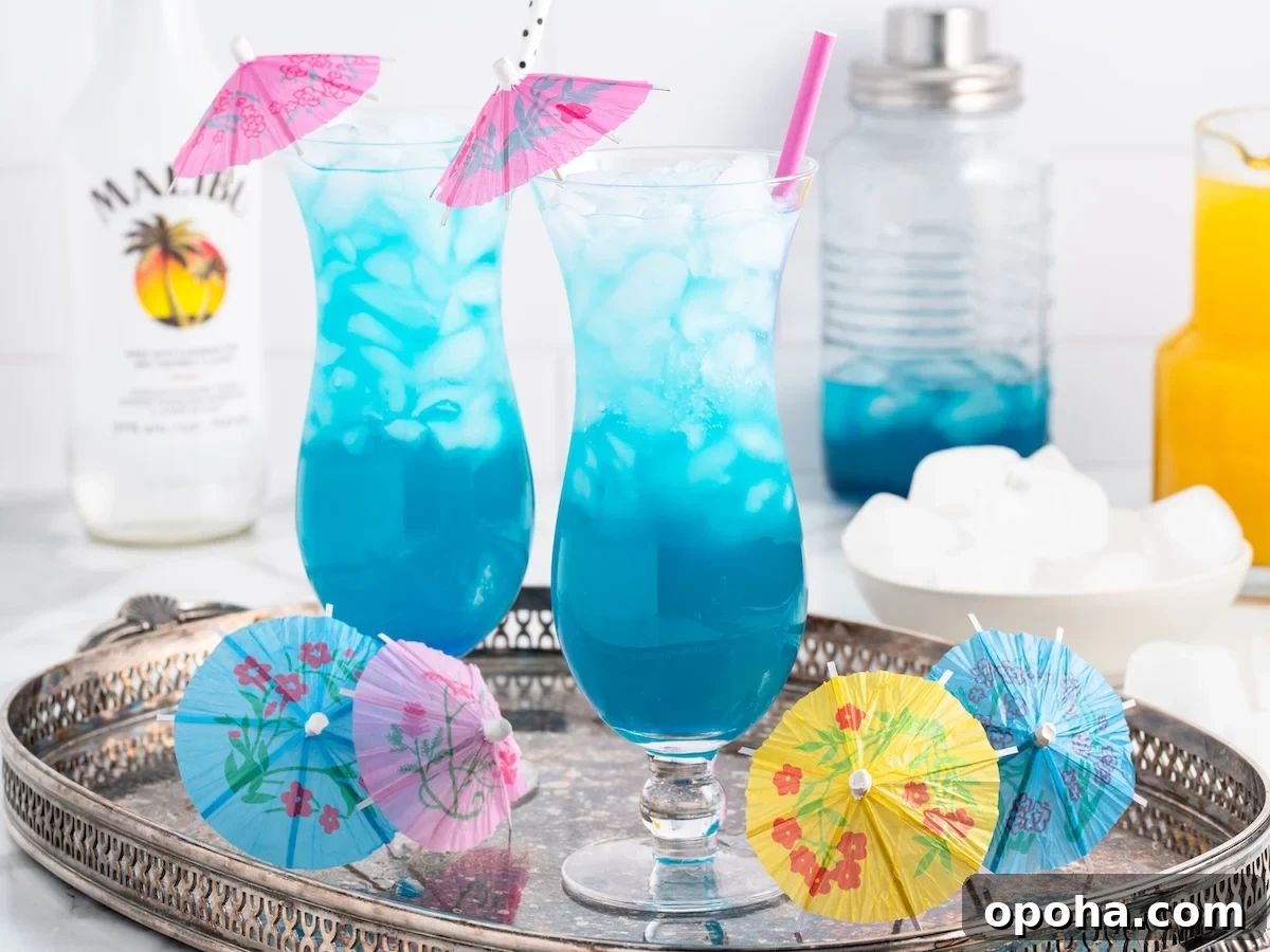 Blue ocean drink recipe in hurricane glasses with pink cocktail umbrellas and a pink straw on a silver tray