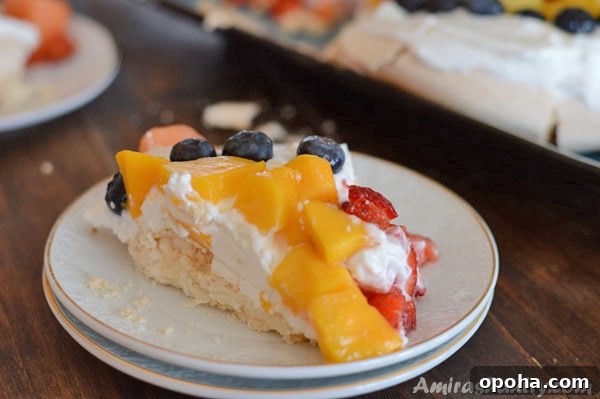 Easter Pavlova Recipe with Fresh Fruit Topping 3 A plate of food with a slice of cake on a table, with Cream and fruits