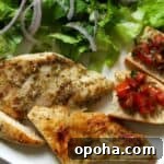 Sauteed chicken breast on plate with salad on side and bread with bruschetta.
