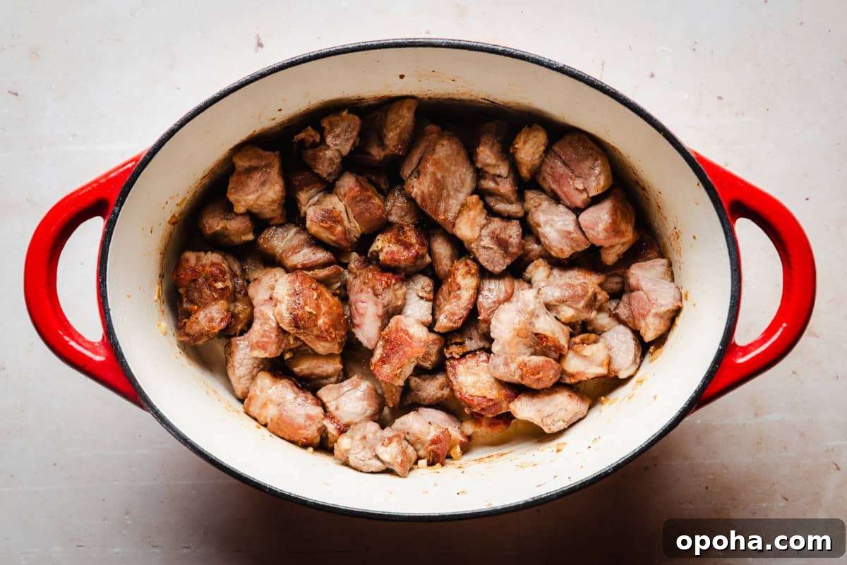 Authentic New Mexican Carne Adovada Recipe 11 Chunks of cooked pork shoulder in a red, oval-shaped cast iron pot.