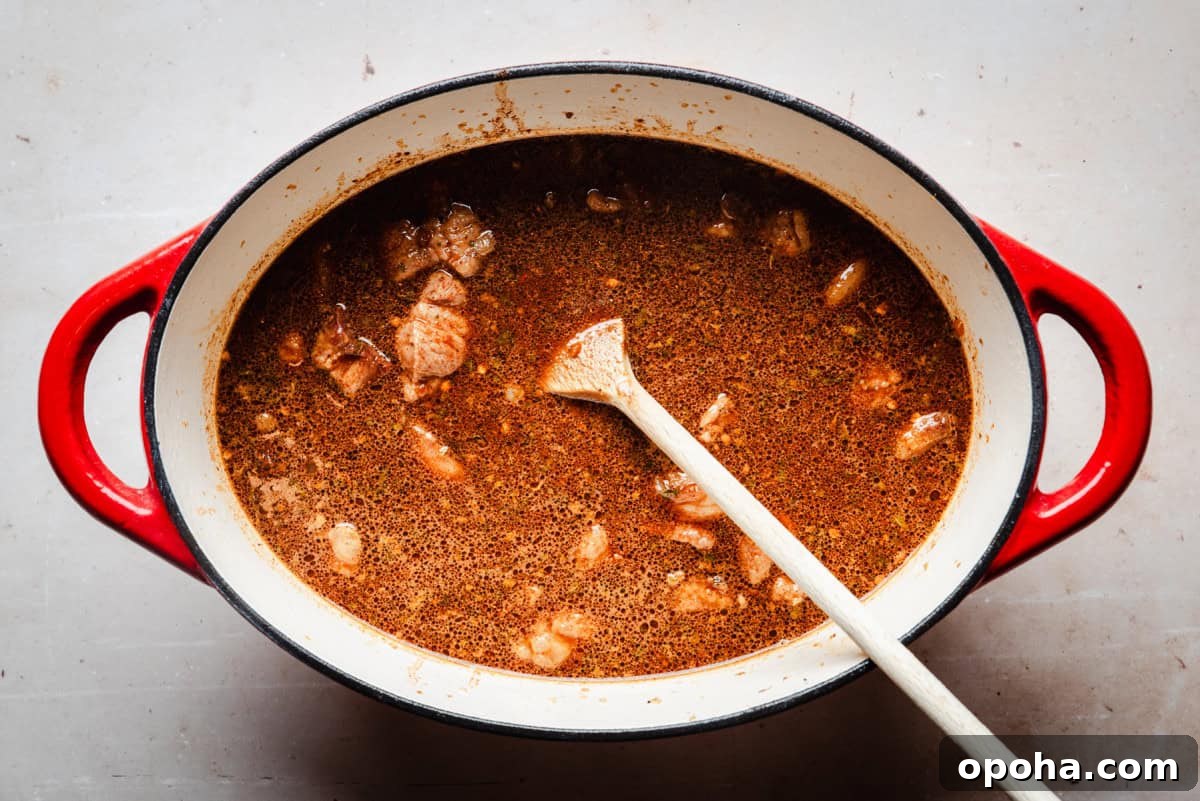 Authentic New Mexican Carne Adovada Recipe 12 A red Dutch oven filled with simmering brown stew containing chunks of pork.