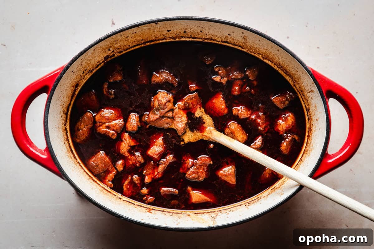 Authentic New Mexican Carne Adovada Recipe 13 A red Dutch oven filled with a rich, dark stew, containing chunks of pork submerged in a thick, brown sauce.