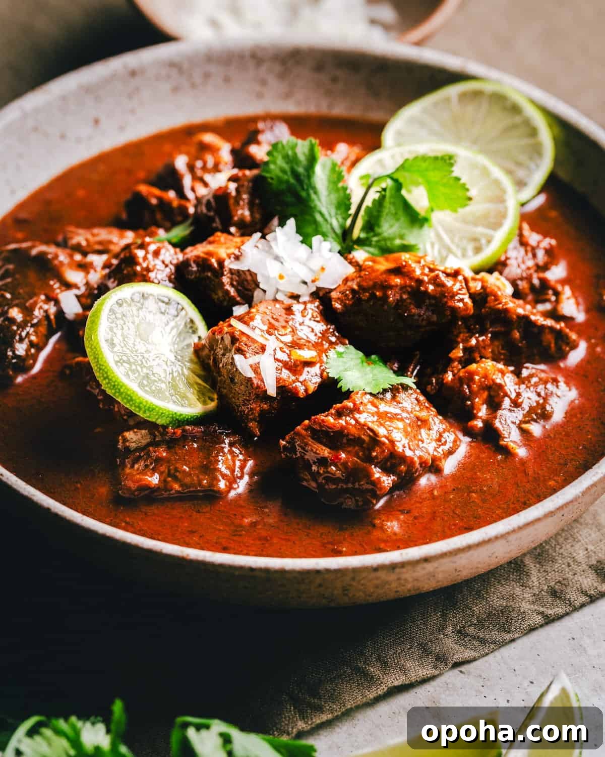 Authentic New Mexican Carne Adovada Recipe 15 A bowl of rich Carne Adovada in a red sauce, garnished with sliced lime, fresh cilantro, and a sprinkle of white rice.