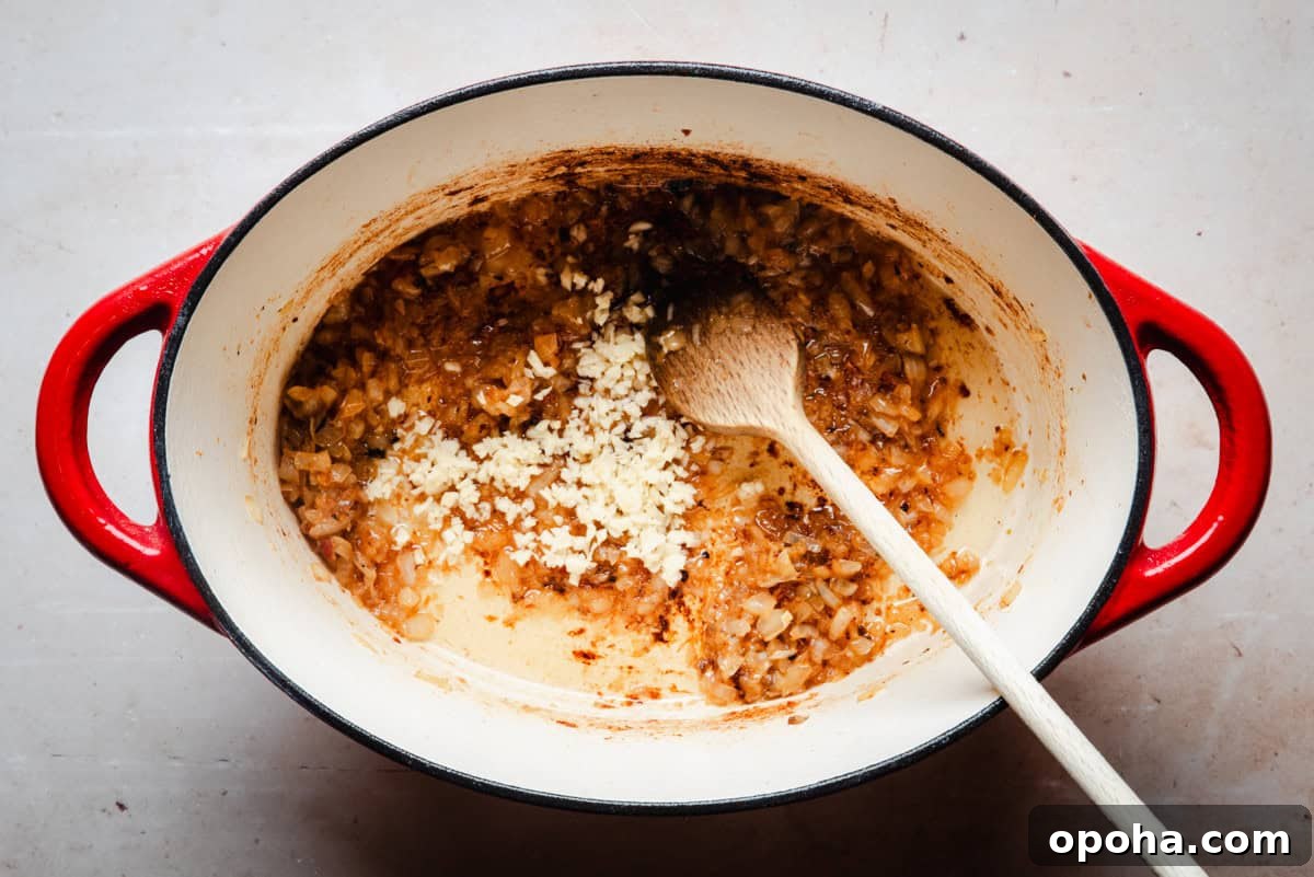 Authentic New Mexican Carne Adovada Recipe 8 Minced garlic being added to sautéed onions in a pot.