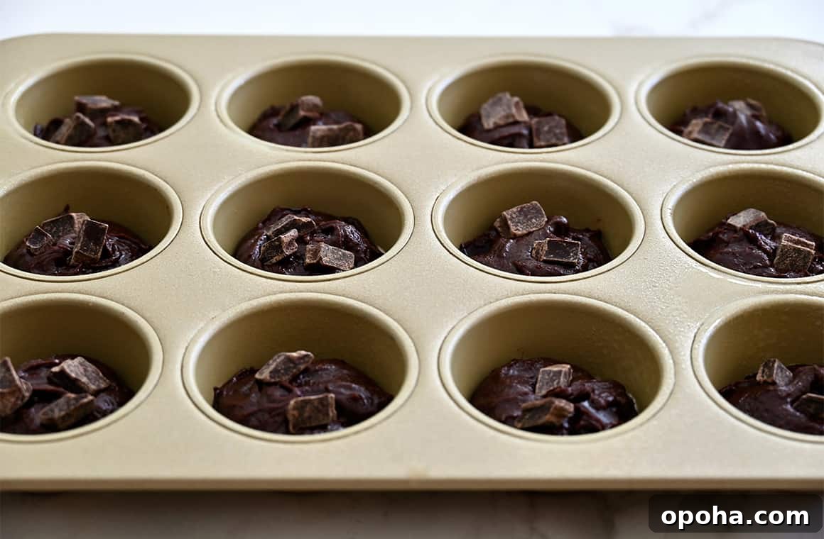Fudgy From-Scratch Brownie Cupcakes Recipe 5 A muffin pan containing chocolate batter topped with chocolate chunks