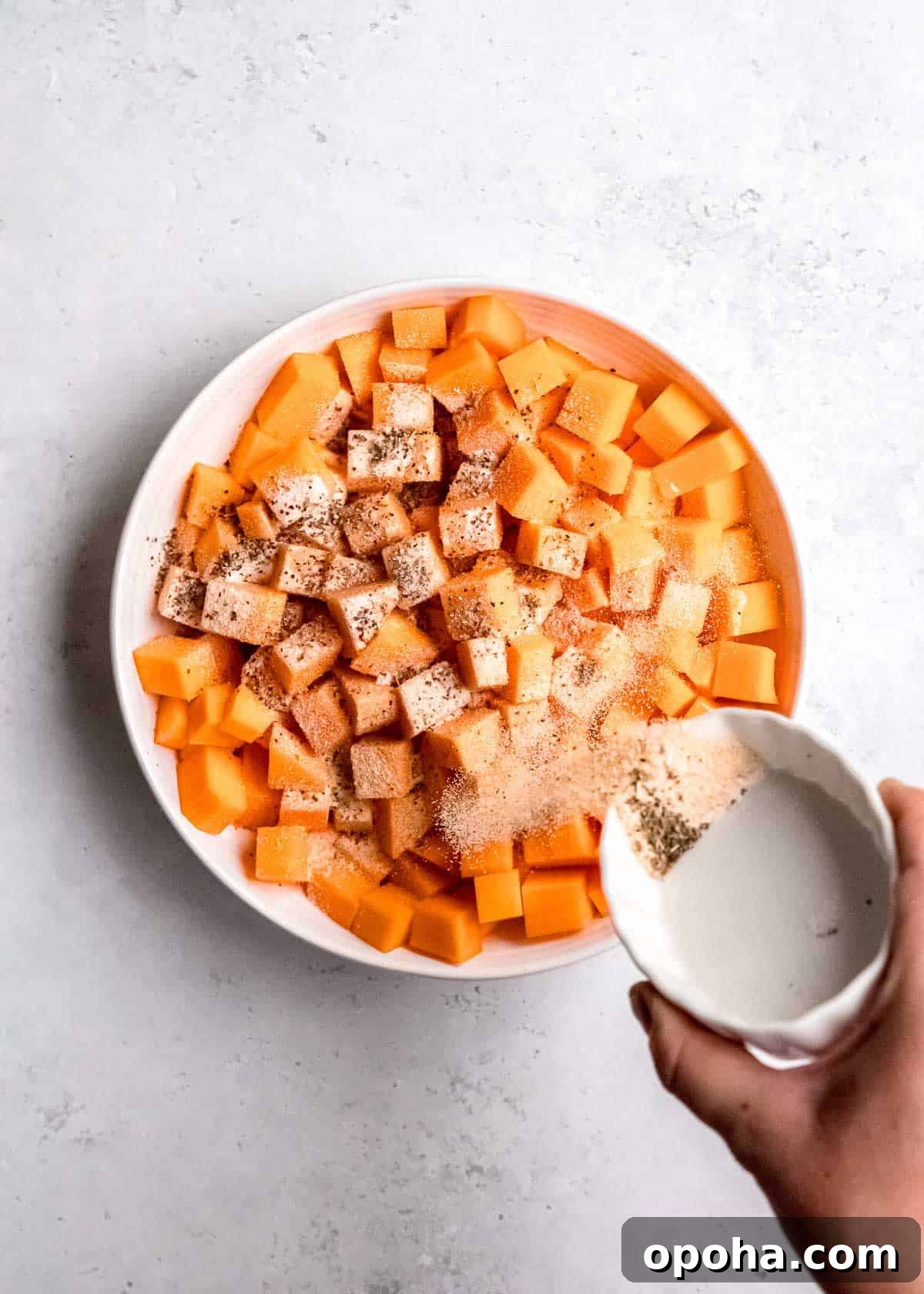 adding seasoning to cubed butternut squash in white bowl