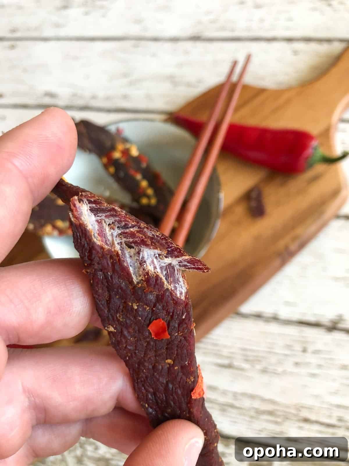 Sesame-Glazed Venison Jerky Recipe: Savory Sweet Game Meat Snack 8 venison jerky bent in half showing it is finished drying by the white fibers and cutting board in background
