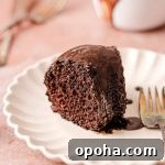 A slice of chocolate cake with chocolate glaze on a plate with a fork.