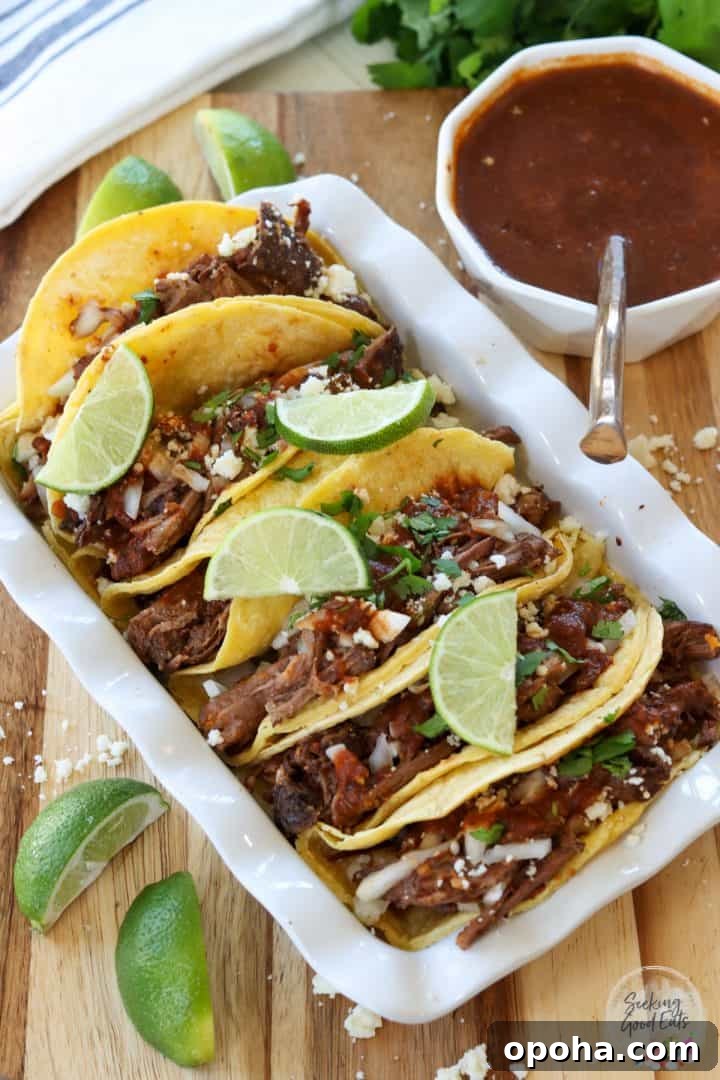 Birria tacos served with consomme and garnished with limes, cilantro, and queso fresco cheese.